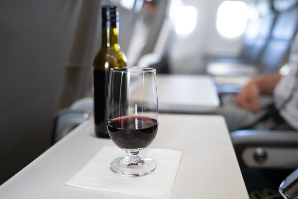 A glass of red wine and a small bottle on a table of a passenger in an airplane